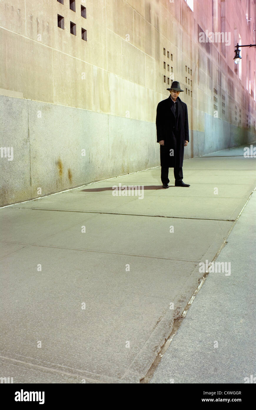 Ein Mann in einen Mantel und heiß gegen eine Betonwand auf dem Bürgersteig in New York City. Stockfoto