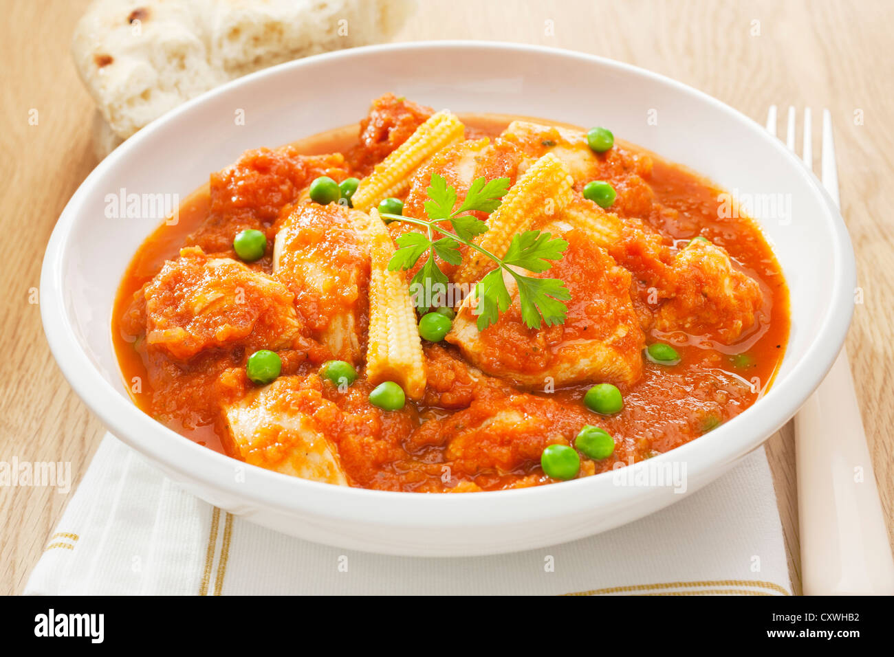 Hähnchen geschmort mit Tomaten, Erbsen und Babymais mit weichem Brot serviert. Stockfoto