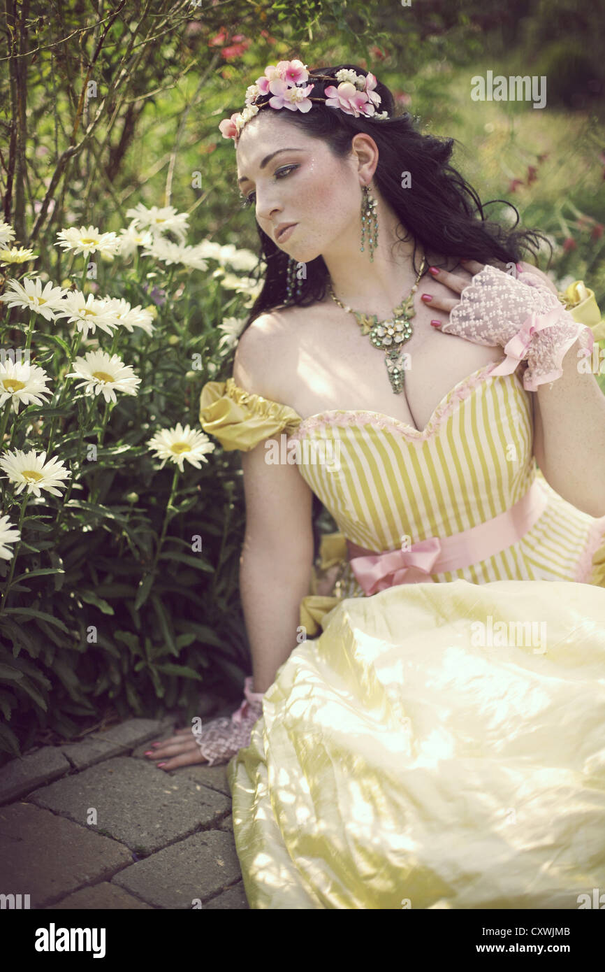 Eine junge Brünette Frau mit Blumen im Haar tragen fancy gelbes Kleid im Sommer sitzen von Gänseblümchen Stockfoto