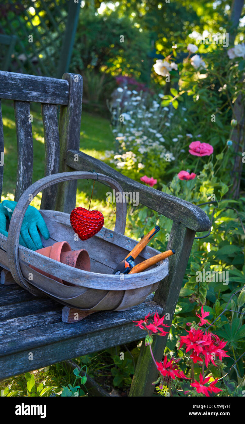 Rustikale Garten Stuhl im sonnigen Blumengarten mit traditionellen Trug, Garten-Accessoires und Herzens Emblem Dekoration Stockfoto