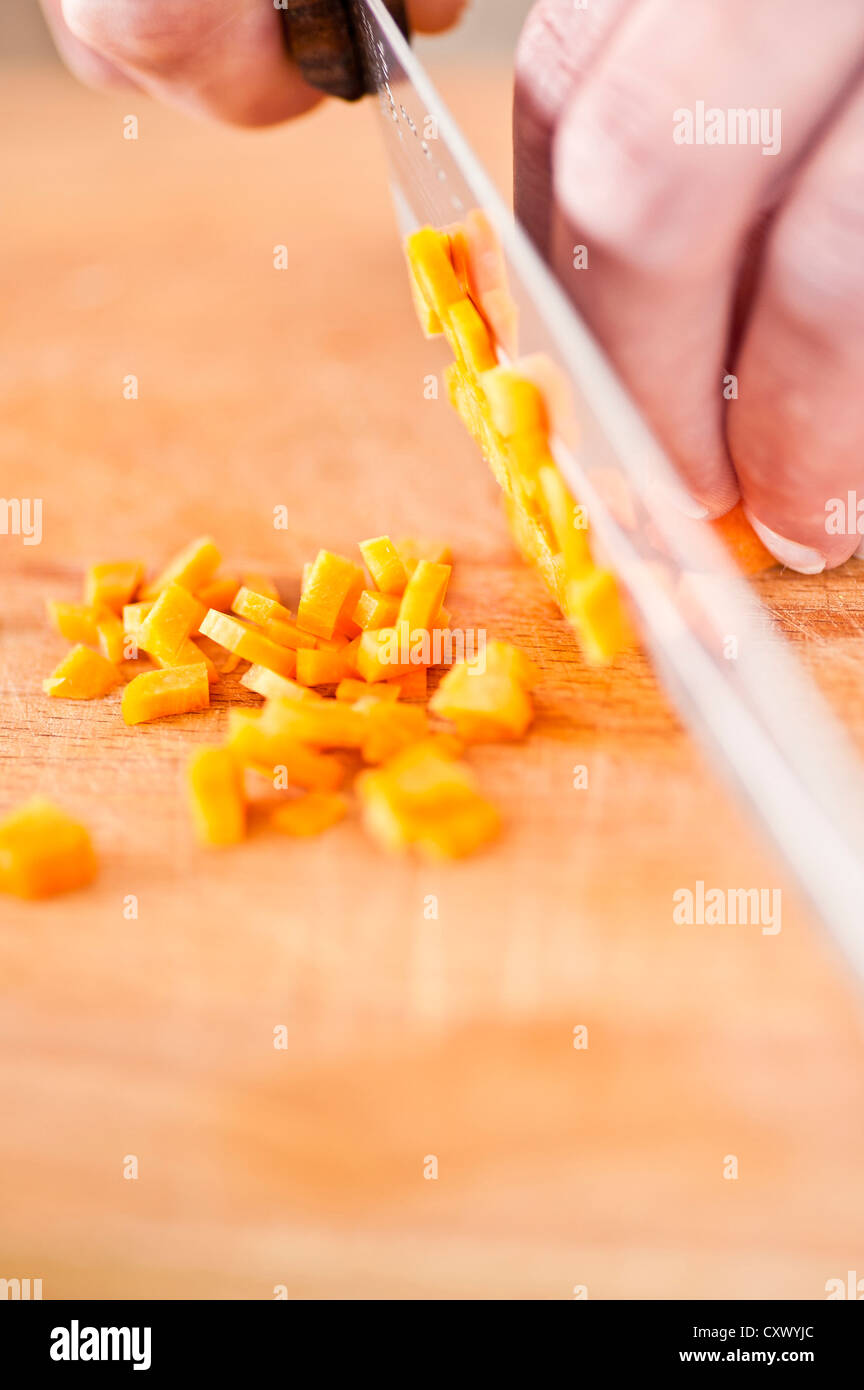 Nahaufnahme von Karotten wird von einem Koch auf einem Holzbrett gehackt Stockfoto