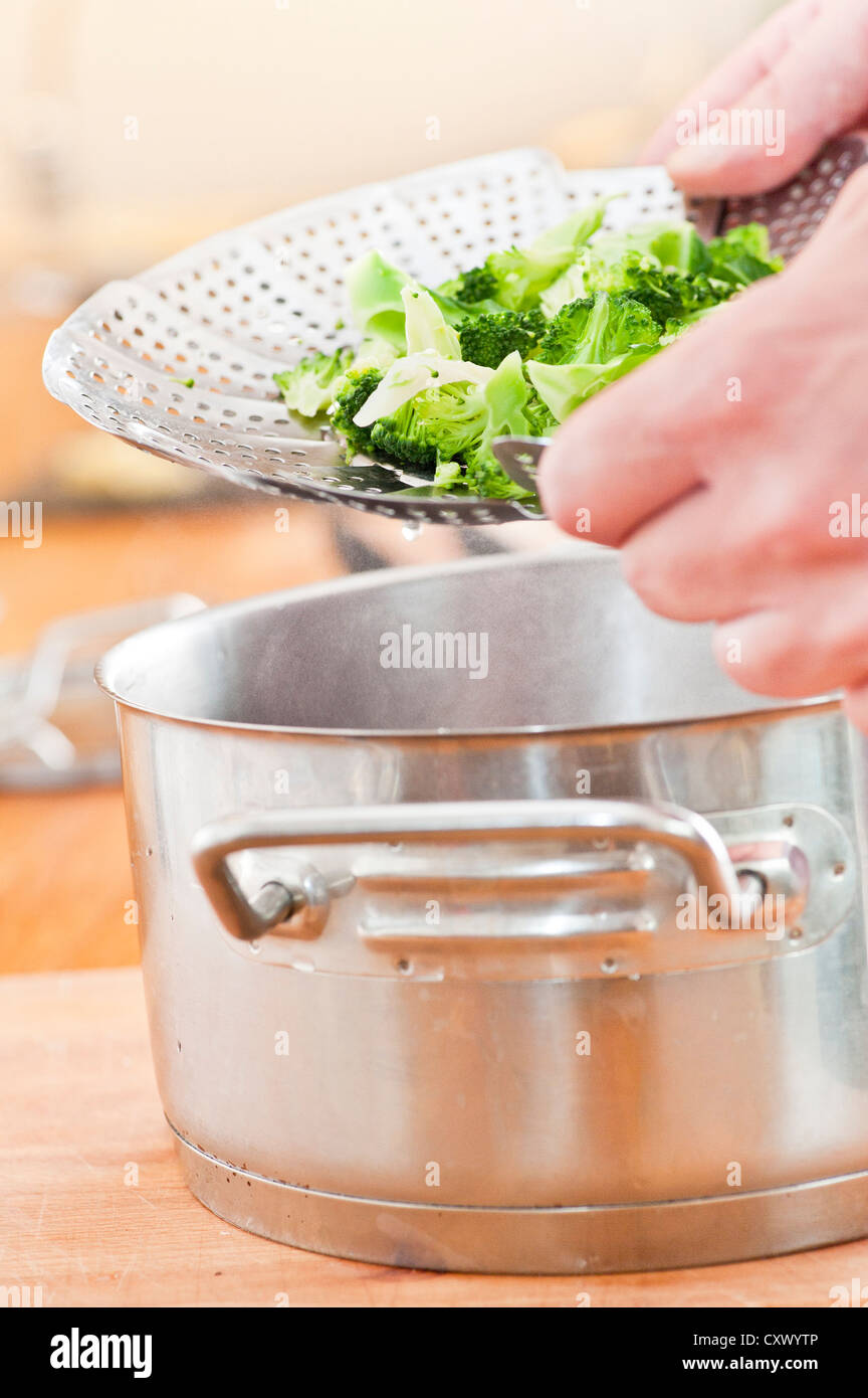 Nahaufnahme des Menschen kochen Brokkoli, bereitet das Gemüse in einen Topf mit einem Dampfer utensil Stockfoto
