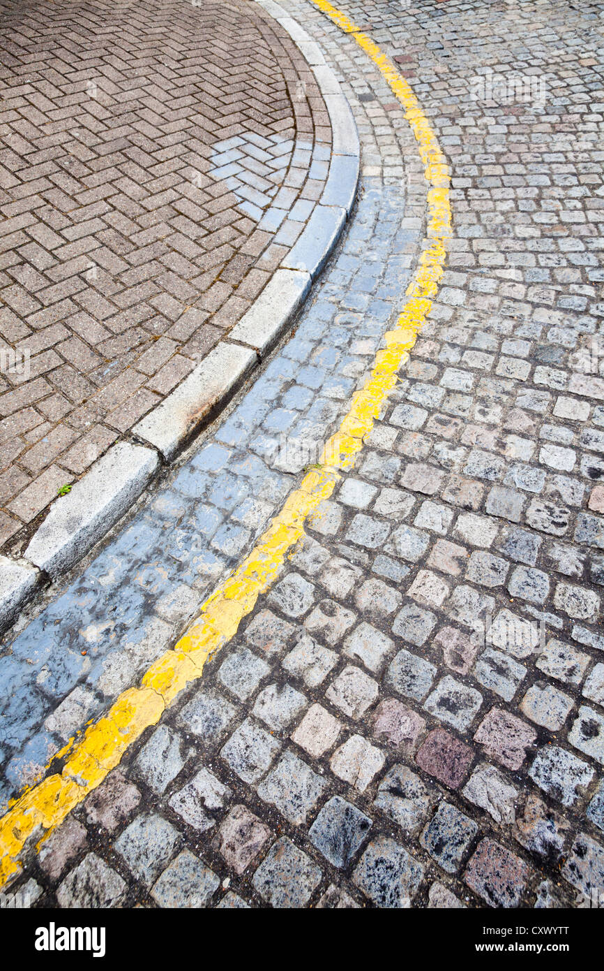 Gelbe Linie Fahrbahnmarkierungen auf gepflasterten Straße Ecke bändigen, Großbritannien Stockfoto