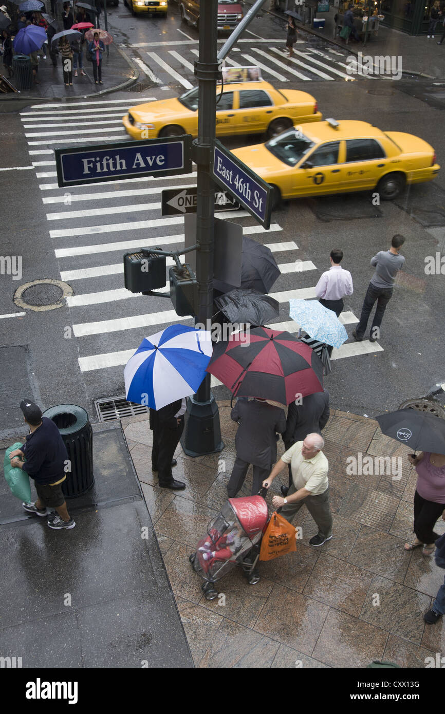 Geschäftsleute in Anzügen haben eine Konferenz unter Sonnenschirmen an der 5th Avenue & 46. St. an einem regnerischen Tag in Manhattan. Stockfoto