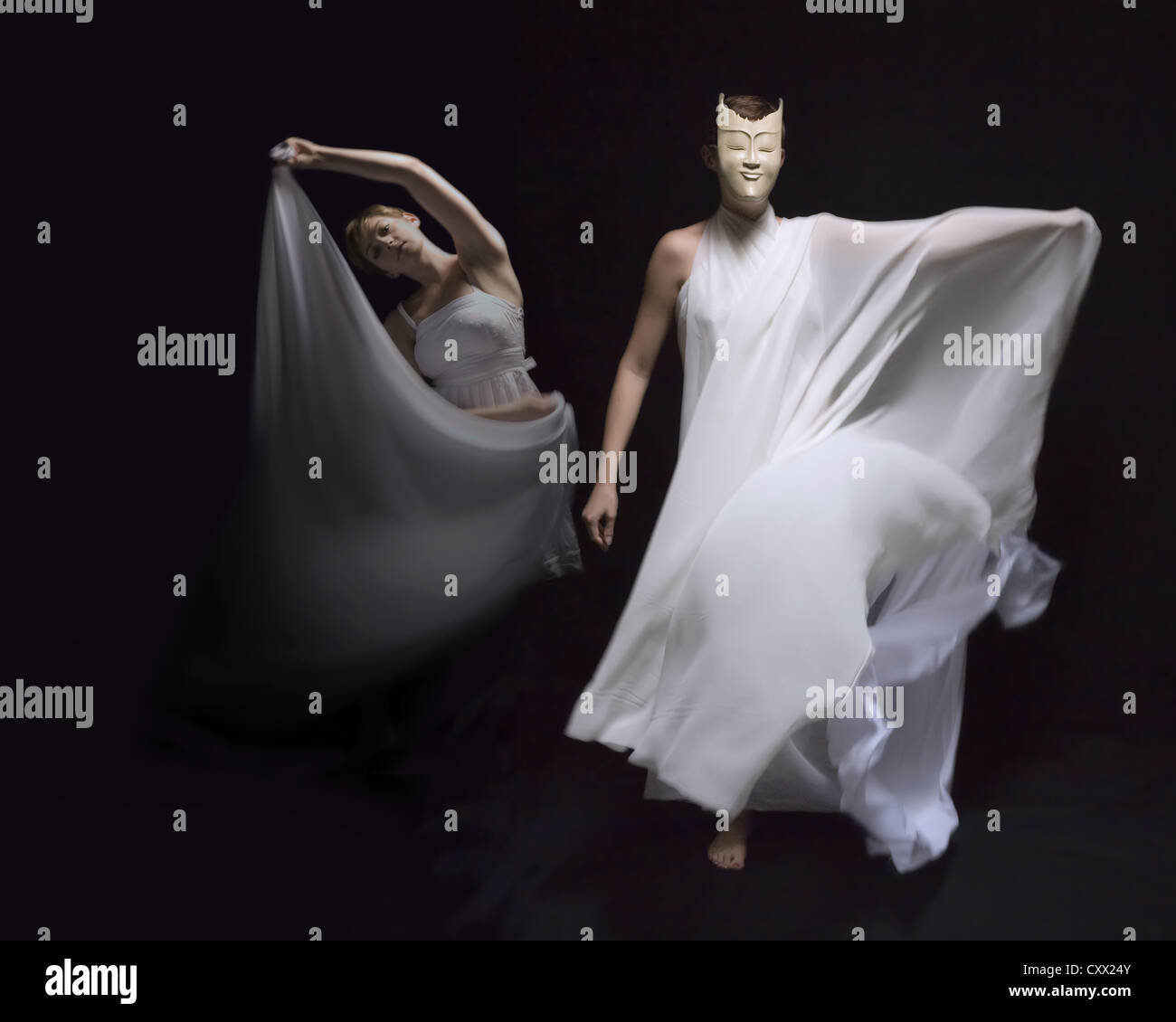 Zwei Tänzerinnen in fließenden weißen Kleider führen unter dramatische Beleuchtung inmitten von schwarzem Hintergrund Stockfoto