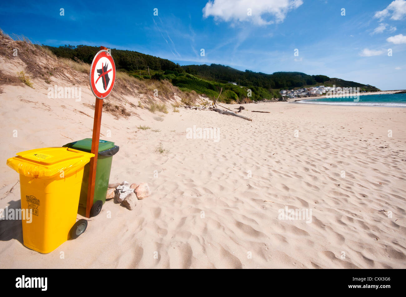 Grüne und gelbe Kunststoffrolle Behälter auf einem sauberen spanischen Strand mit Dünen und einer ruhigen Bucht in der Ferne. Bares, Galizien. Stockfoto