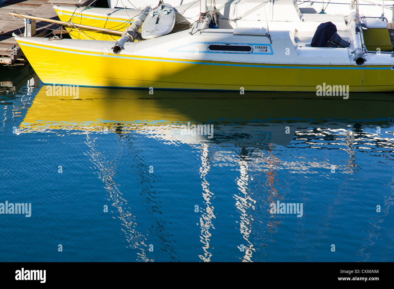 Rumpf und Mast von einem gelben Katamaran im Wasser gespiegelt. Stockfoto