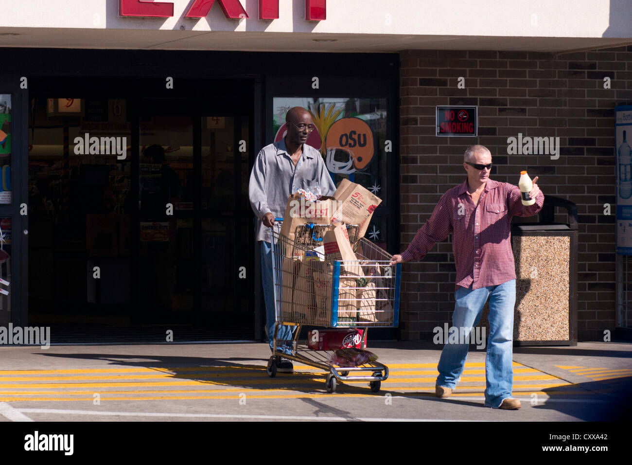 Ein schwarzer Mann und einem kaukasischen Mann schieben und ziehen einen geladenen Einkaufswagen aus einem Supermarkt in Oklahoma City, Oklahoma, USA. Stockfoto