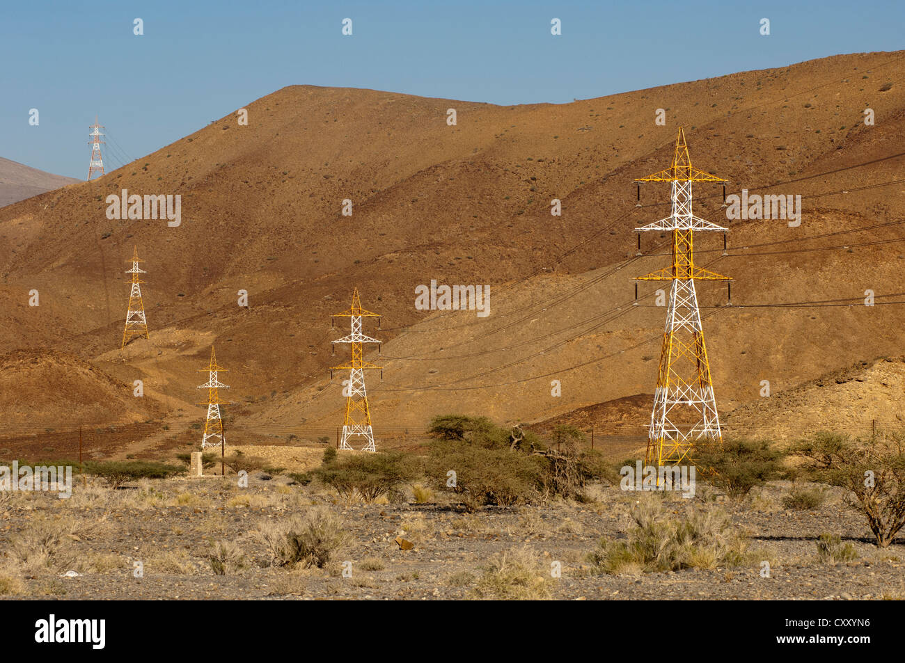 Hochspannungskabel mit roten und weißen Pylone überqueren die kargen Hängen des Al-Hajar-Gebirge, Sultanat von Oman Stockfoto