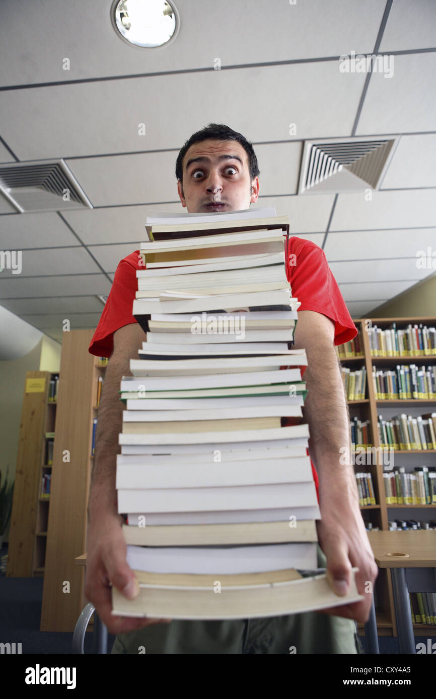 Student mit einem Stapel Bücher in einer Universitätsbibliothek Stockfoto