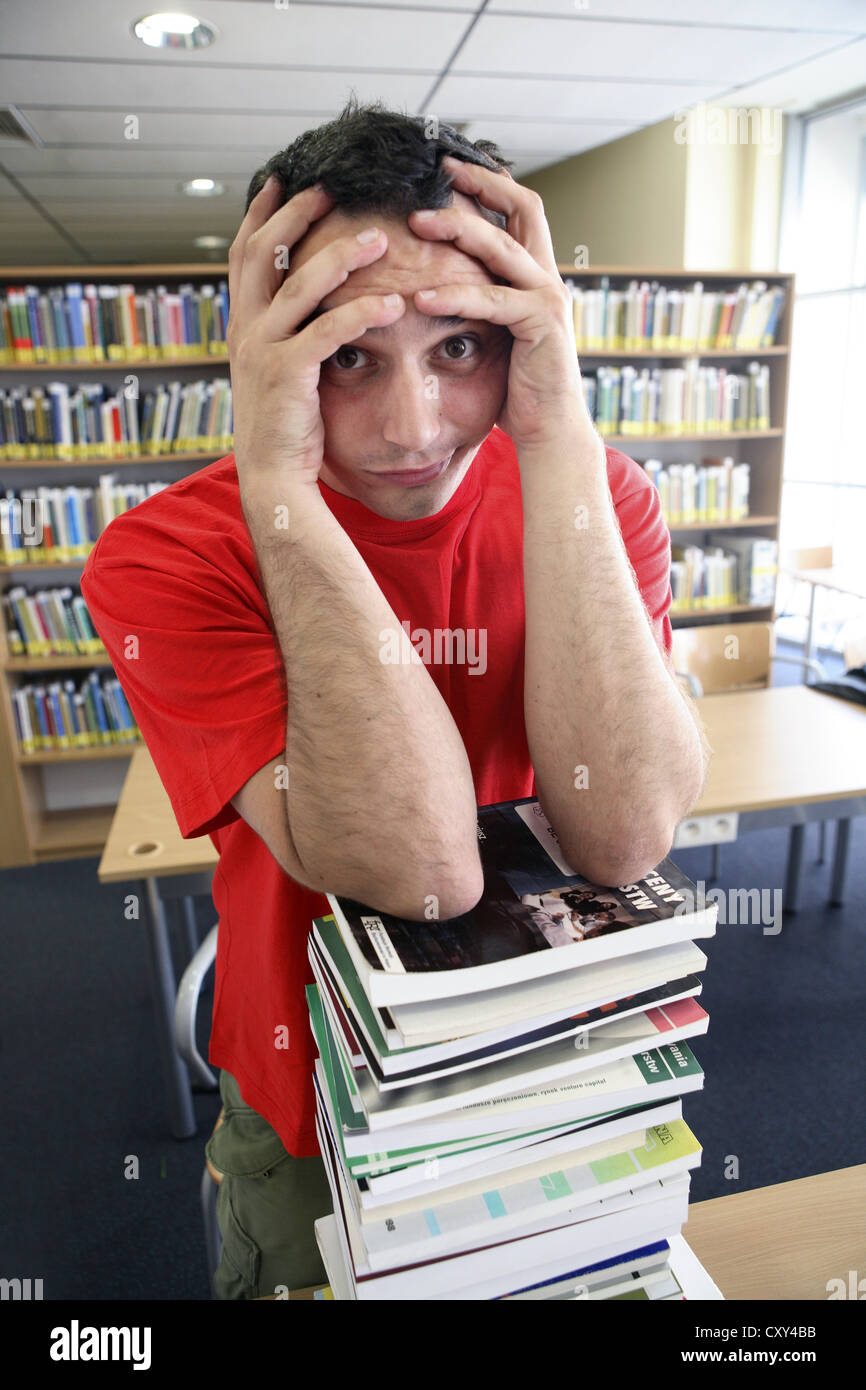 Verzweifelten Schüler basierend auf einen großen Stapel Bücher, Universitätsbibliothek Stockfoto