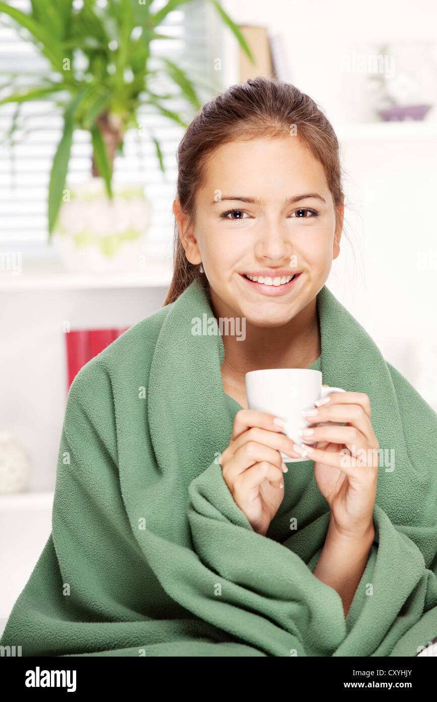 hübsche junge Frau trinkt Tee zu Hause bedeckt mit Decke Stockfoto