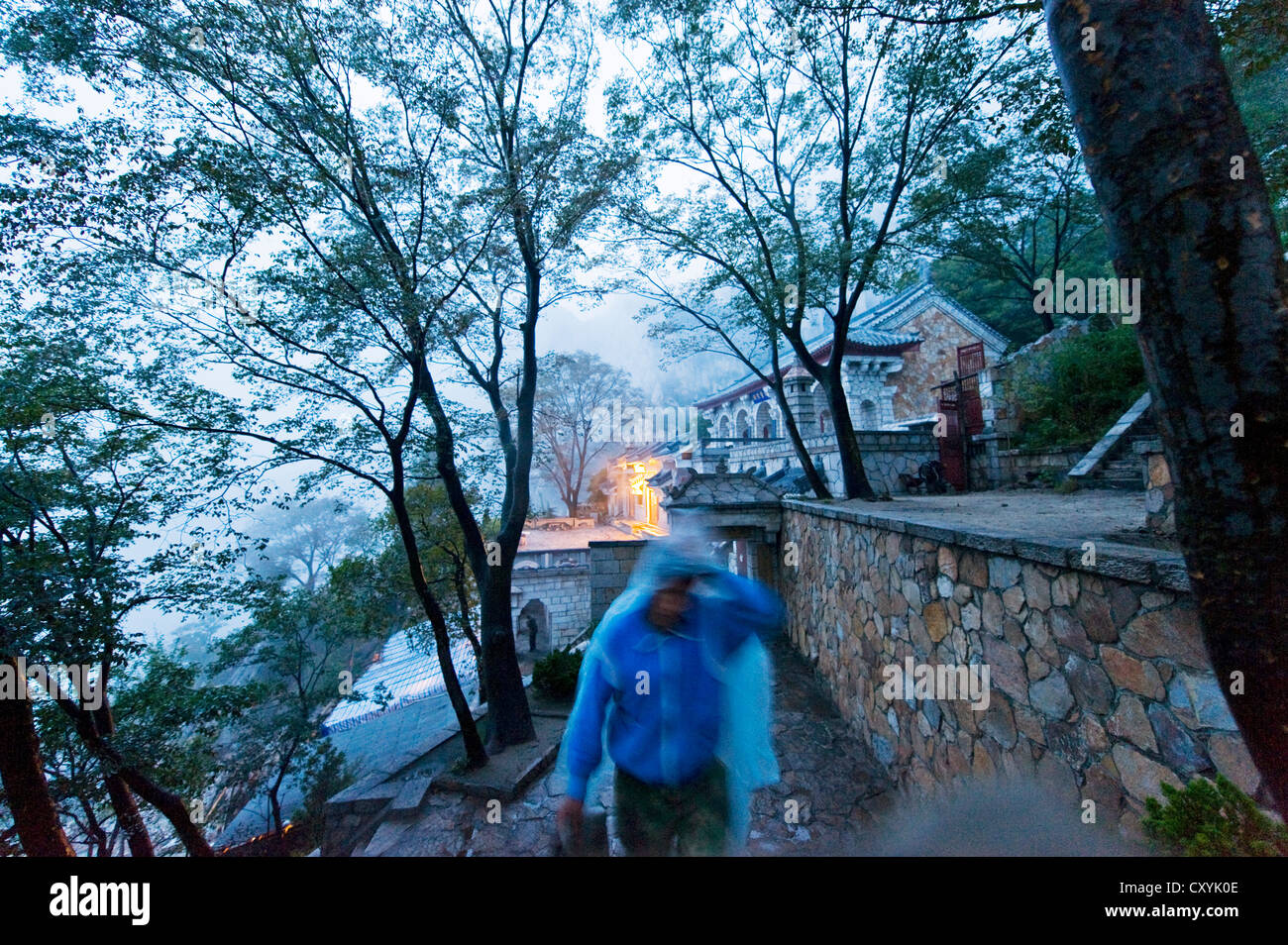 Ein Poncho bedeckt Person zu Fuß im Regen im San Huang Zhai Kloster auf dem Song-Berg, China Stockfoto