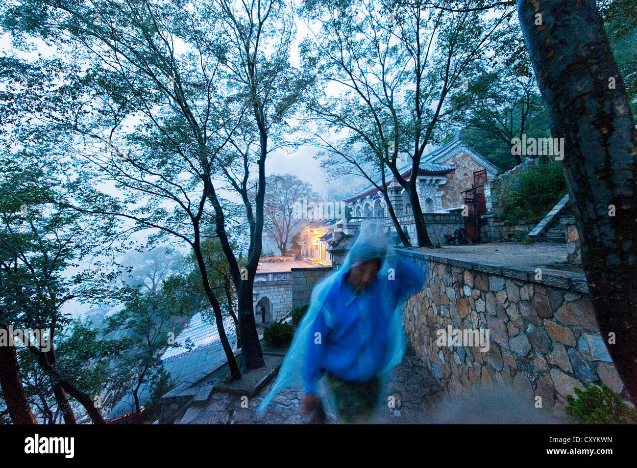 Ein Poncho bedeckt Person zu Fuß im Regen im San Huang Zhai Kloster auf dem Song-Berg, China Stockfoto