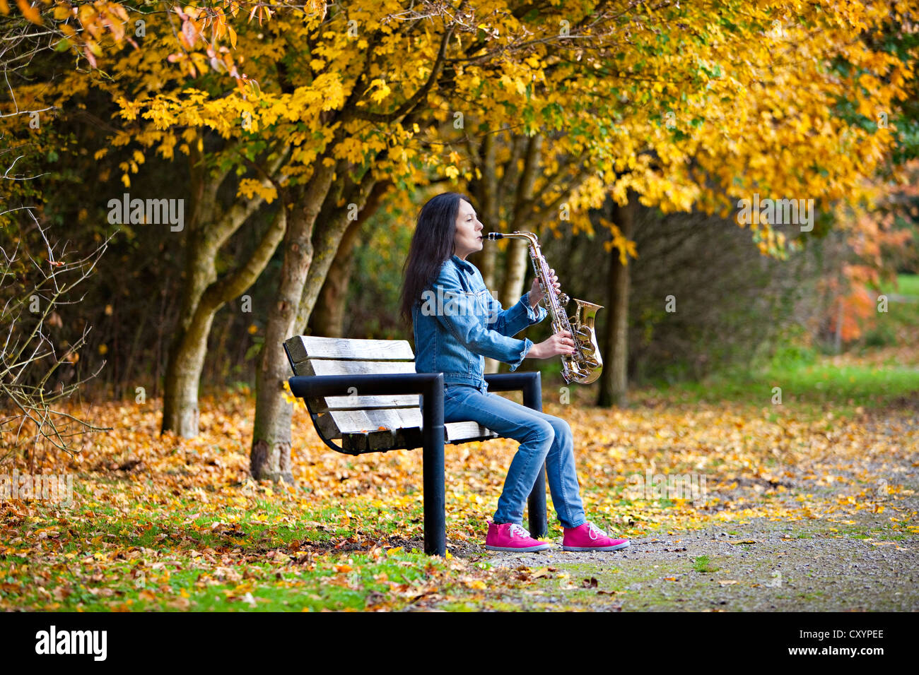 Frau sitzt auf der Bank im Park, Saxophon Stockfoto