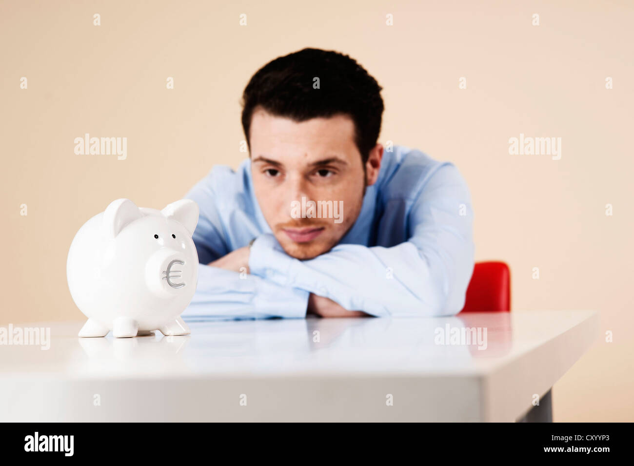 Junger Mann sitzt nachdenklich vor ein Sparschwein Stockfoto