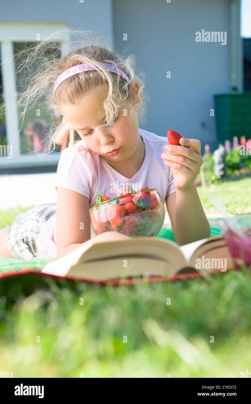 Mädchen mit Erdbeeren und ein Buch im Garten Stockfoto