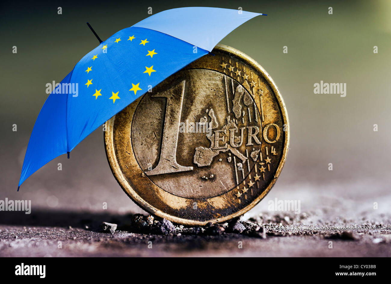 Verbrannte 1-Euro-Münze in der Asche unter einem Regenschirm mit den Stars der Europäischen Union, symbolisches Bild für die Euro-Krise, Euro-Rettungsschirm Stockfoto