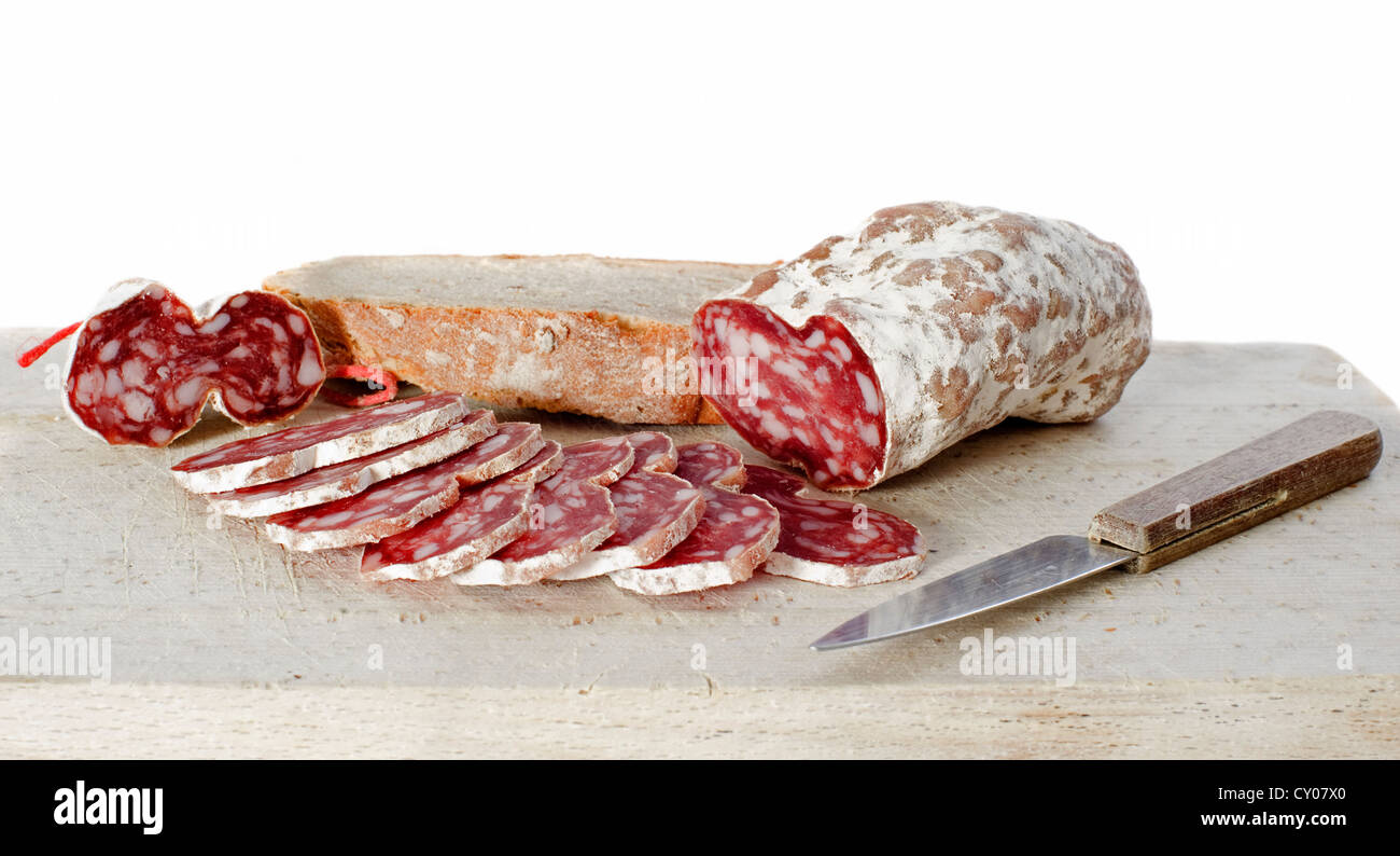 In Scheiben geschnitten französische Saucisson auf Schneidebrett mit Messer vor weißem Hintergrund Stockfoto