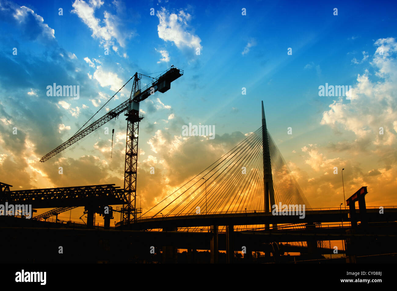 Silhouetten der Baukran und eine Brücke in Dämmerung gegen den bunten Himmel. Stockfoto