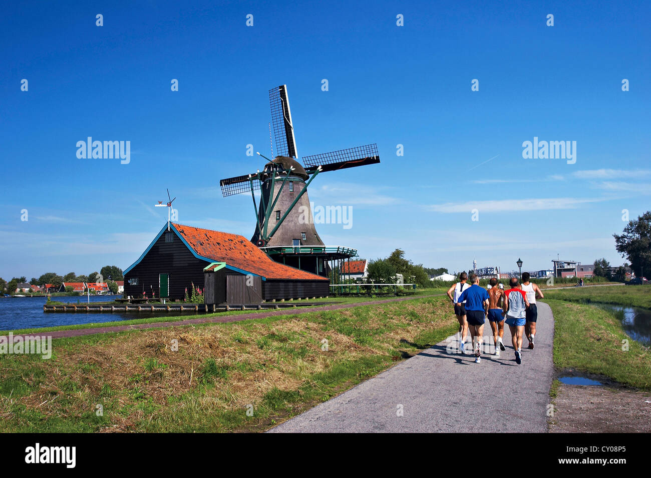 Niederlande, Nordholland, Zaanstad, Zaanse Schans, Windmühlen, Jogger am Weg entlang des Kanals. Stockfoto