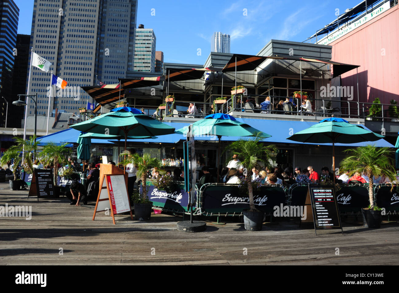 Blauer Himmelsblick auf Financial District Wolkenkratzer, Leute sitzen Essen Seehafen Cafe, Pier 17, South Street Seaport, New York Stockfoto
