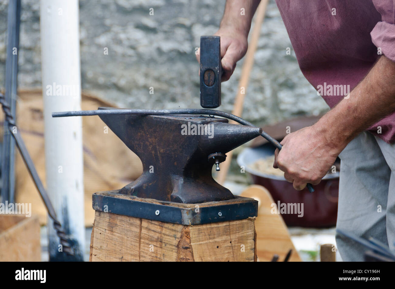 Hufschmied mit Vorschlaghammer in Motion blur zerschlägt mit volle Wirkkraft in ein glühendes Eisen Stab Werkstück auf einem Schmied Amboss Stockfoto