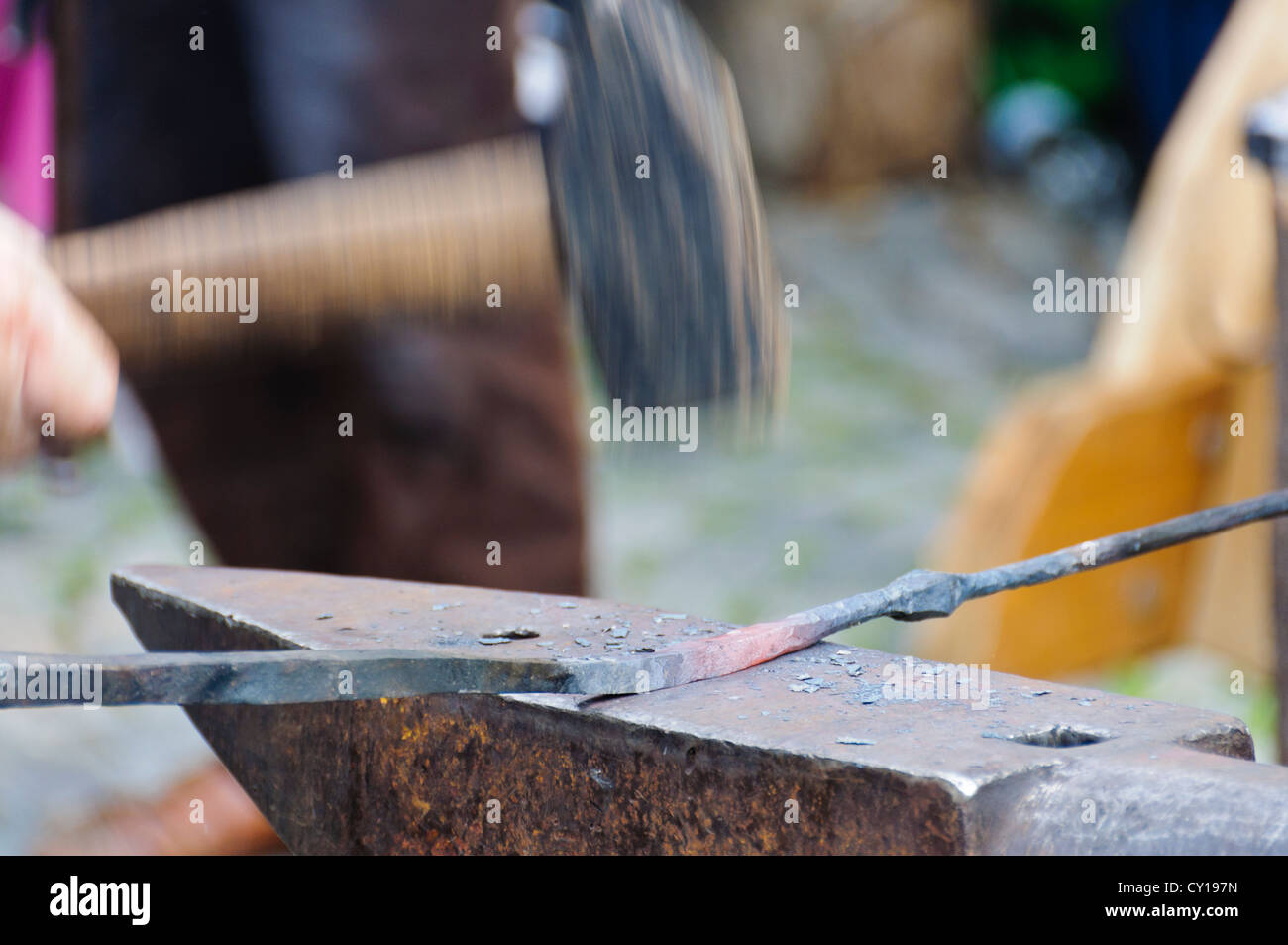 Vorschlaghammer in Motion blur zerschlägt mit volle Wirkkraft in ein glühendes Eisen Stab Werkstück auf einem Schmied Amboss Stockfoto