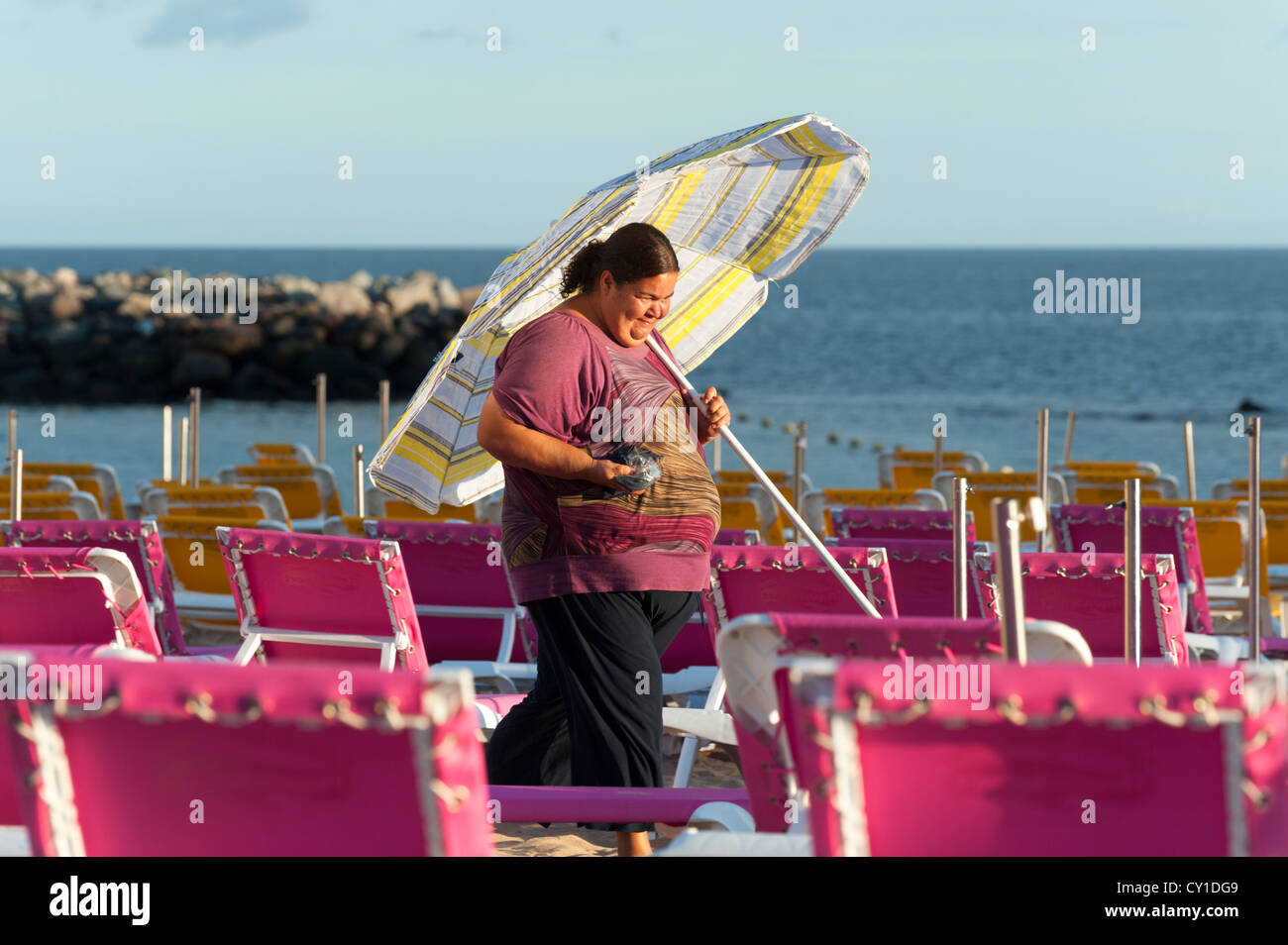 Bunten Liegestühlen am Strand von Playa de Mogan Gran Canaria Kanaren Spanien mit einer Frau mit einem Sonnenschirm Stockfoto
