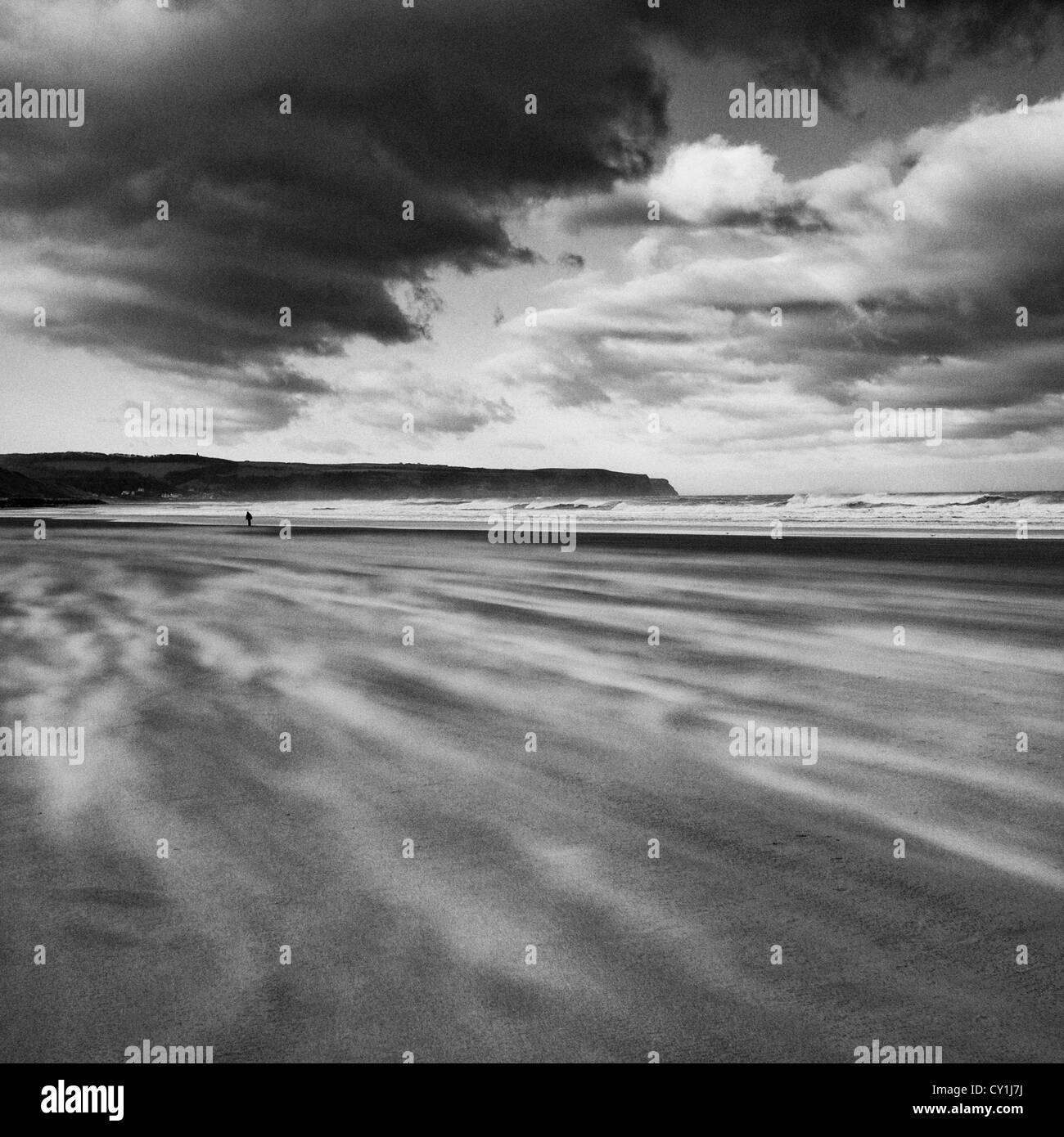 Einsame Gestalt windigen Strand entlang unter stürmischen Himmel in Whitby, North Yorkshire, England Stockfoto