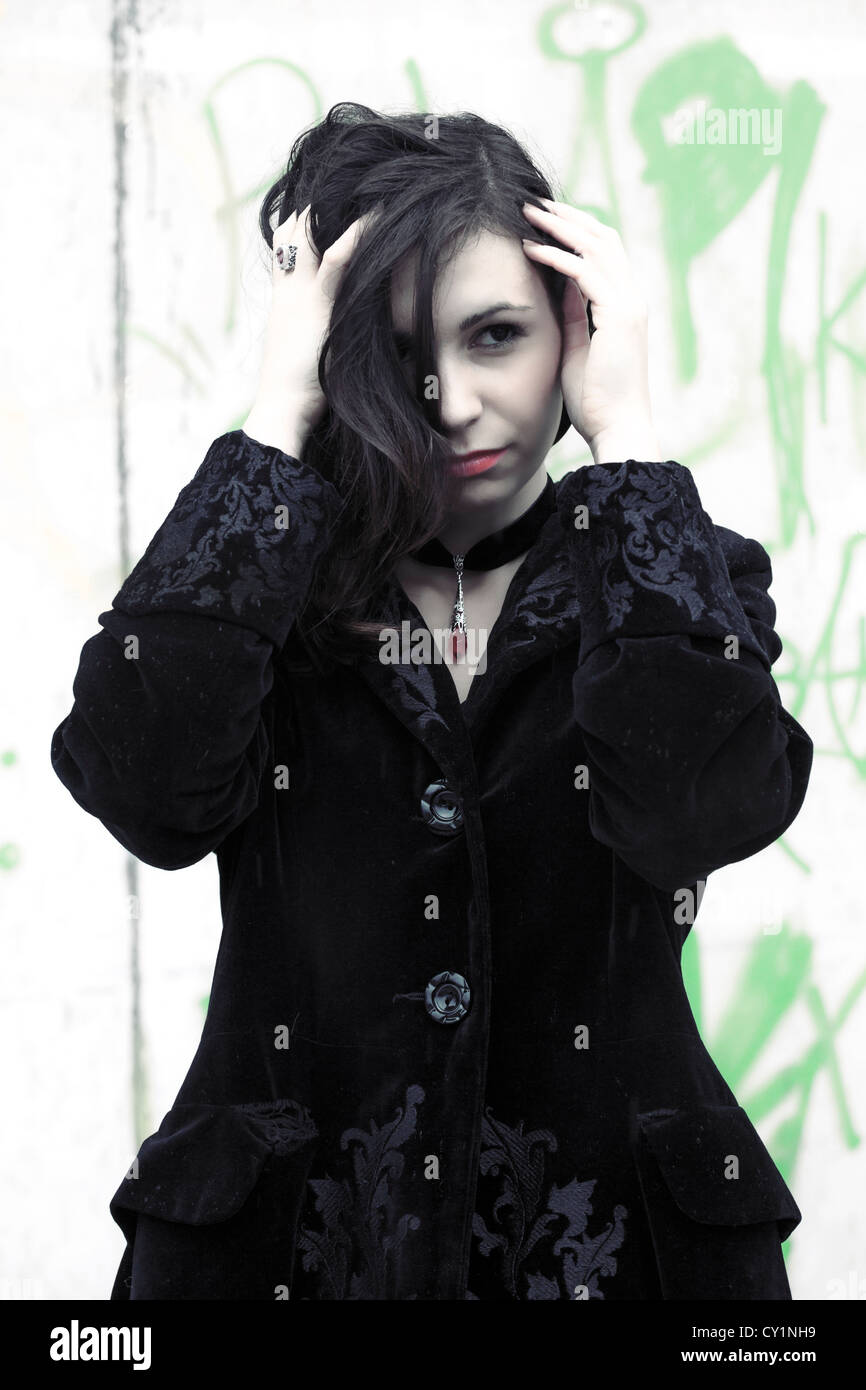 eine Frau in einem schwarzen Mantel vor einer Graffitiwand Stockfoto