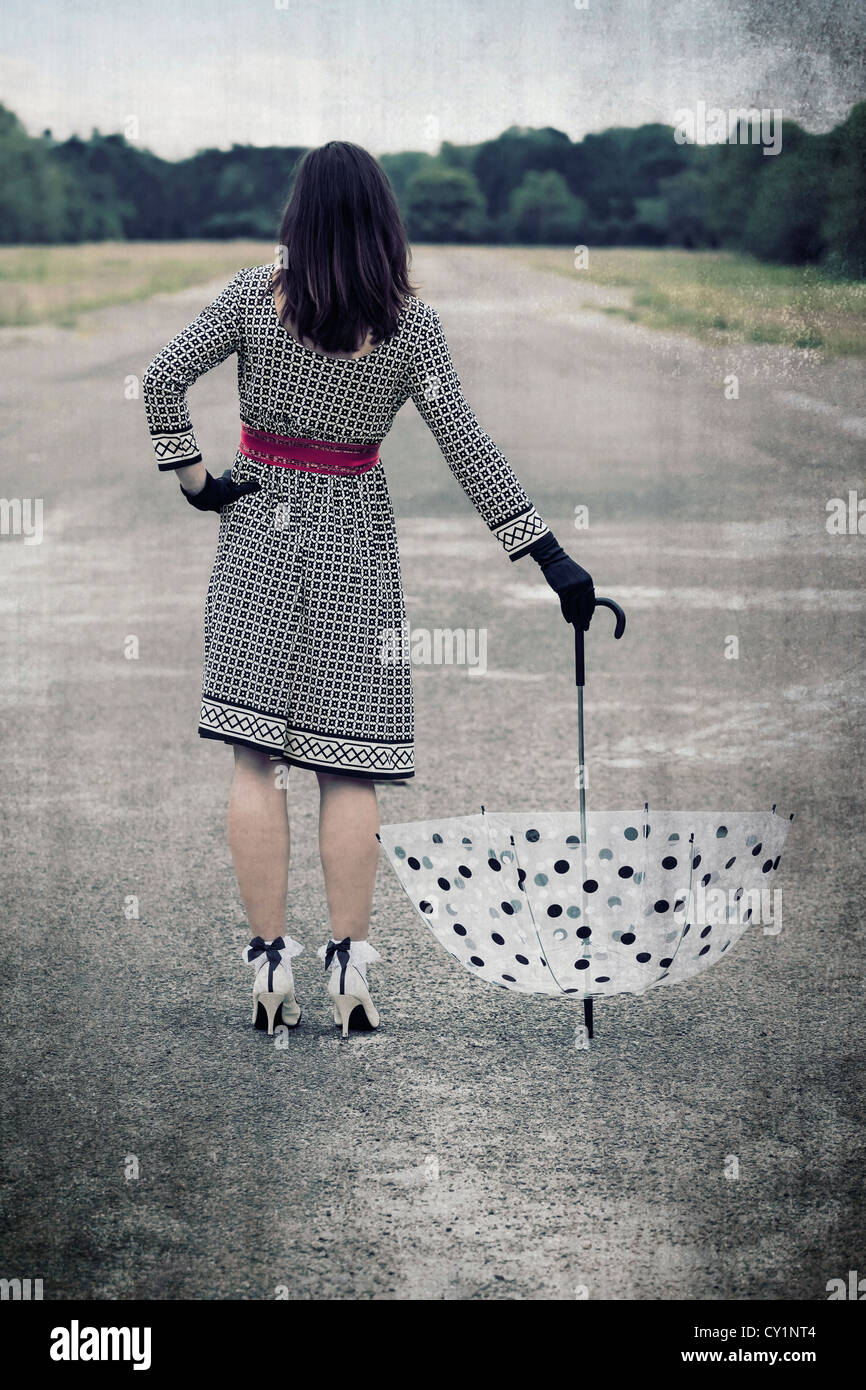 eine Frau steht auf einer Straße und hält einen Vintage Schirm Stockfoto