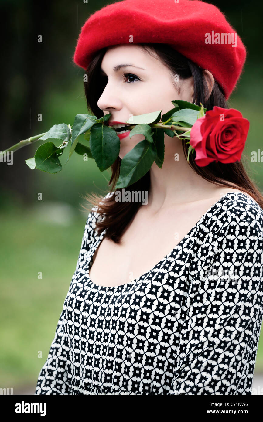 eine Frau in einem schwarzen und weißen Kleid hält, dass eine rote rose im Mund Stockfoto