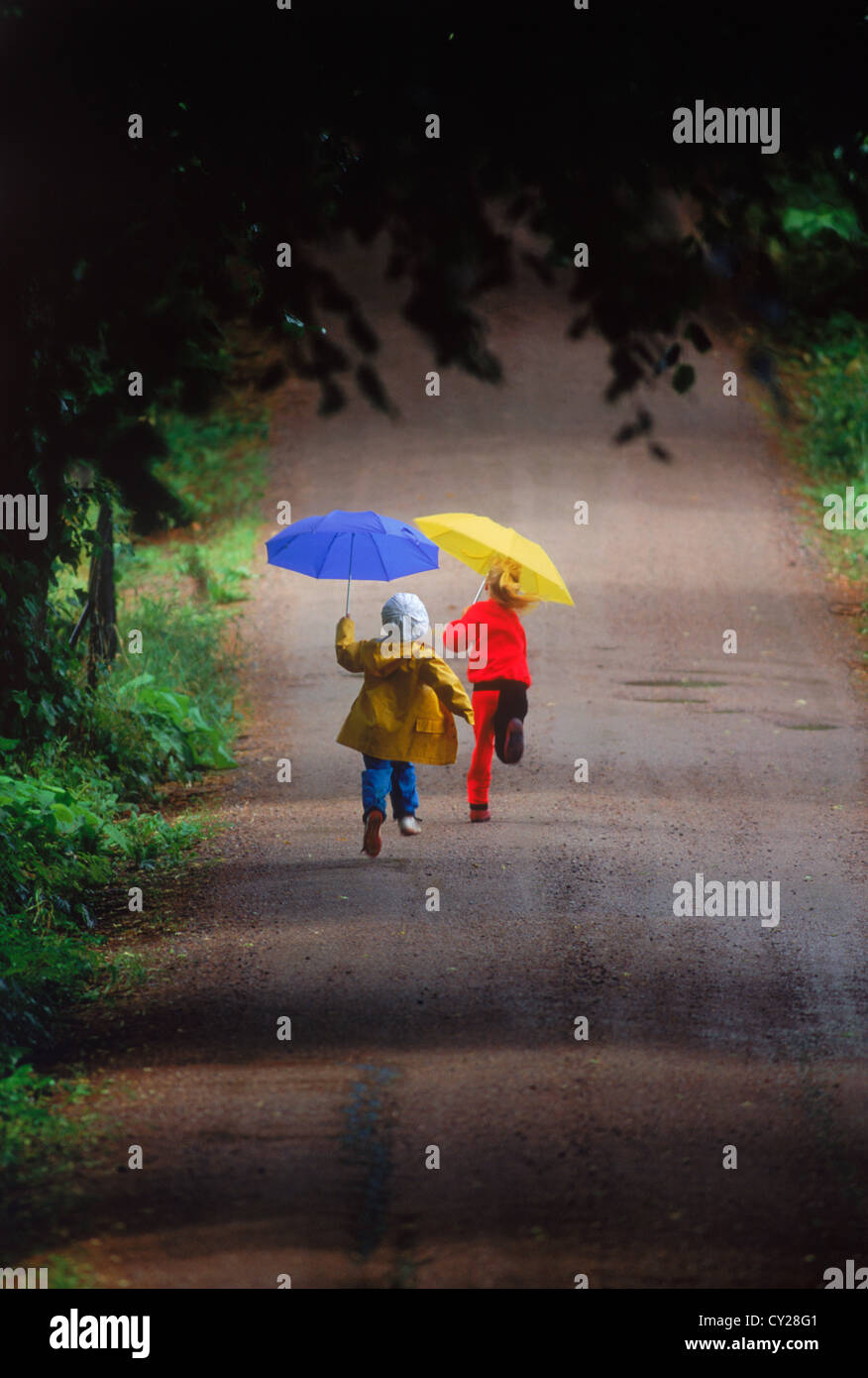 Jungen und Mädchen laufen auf Landstraße in den Regen halten bunte Sonnenschirme Stockfoto