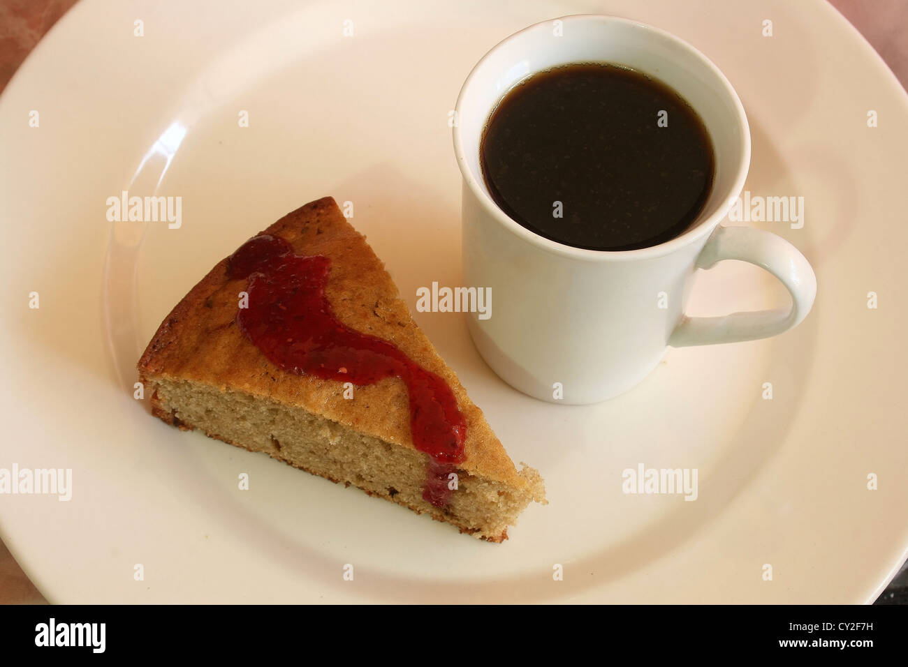 Ein Stück warmen Bananenkuchen mit einem Erdbeer-Topping serviert auf einem weißen Teller mit einer Tasse frisch gebrühten Kaffee Stockfoto