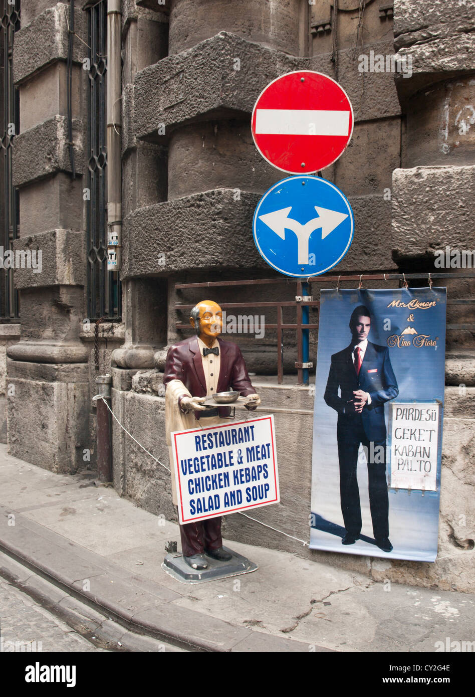 Kontrastierende Schilder an einer Straßenecke, Verkehr Wegweiser, alte Restaurant Werbung und moderne Anzüge zum Verkauf in Istanbul Stockfoto