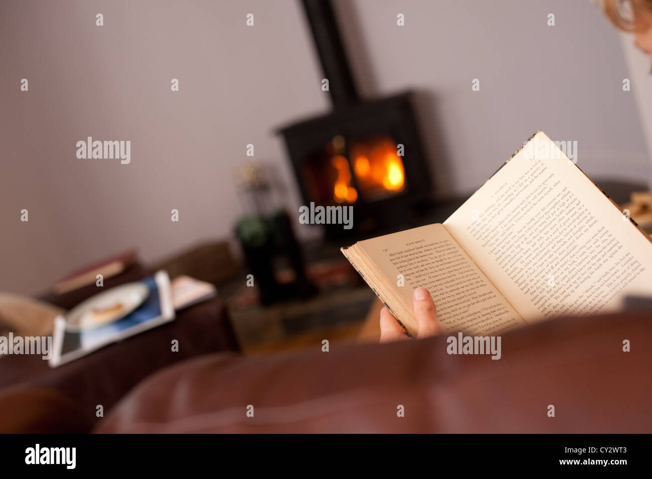 Eine Frau liest ein Buch vor dem Kamin in einem Ferienhaus in Cornwall im winter Stockfoto