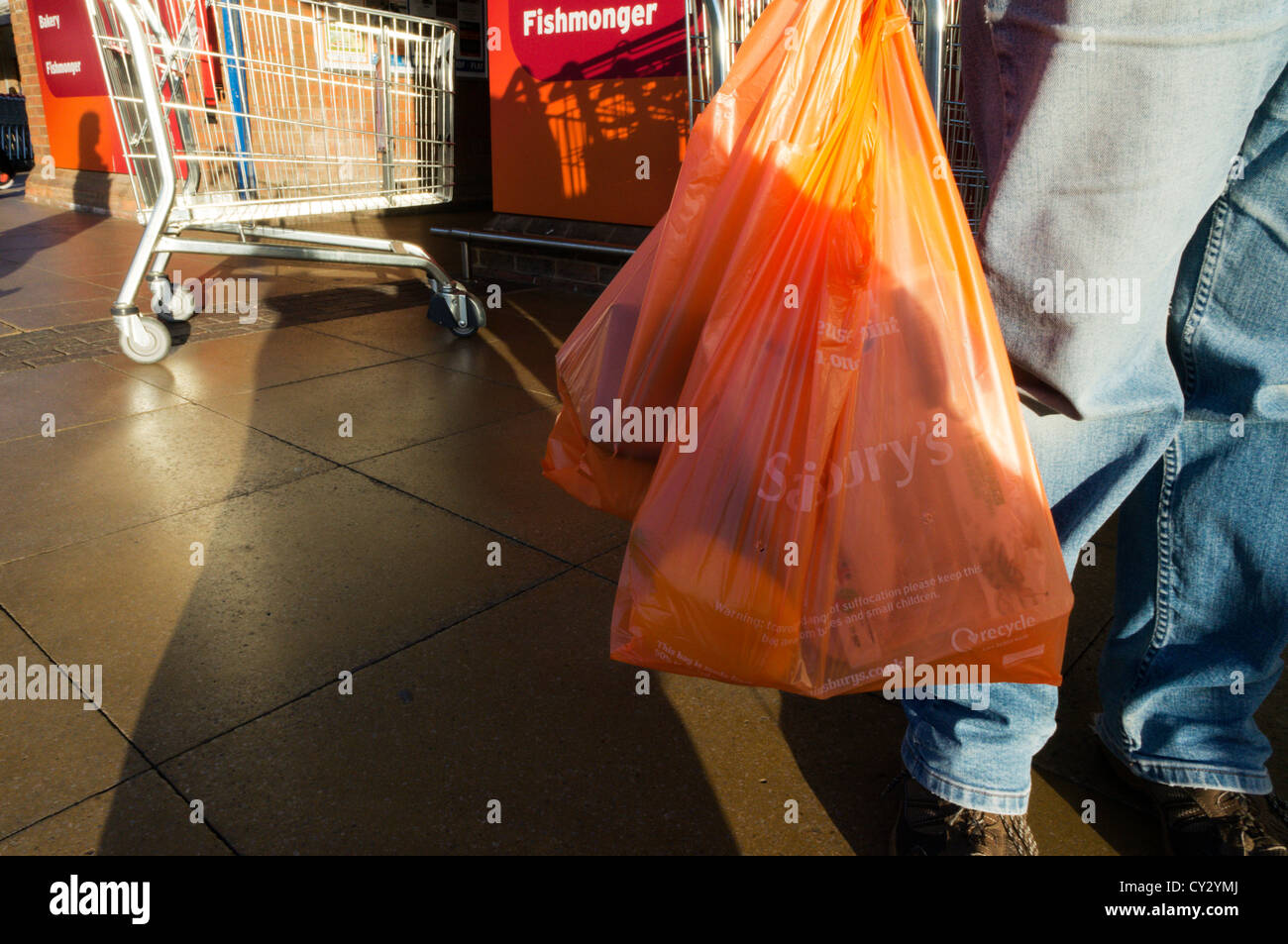 Eine Frau, die trägt Sainsbury Kunststoff-Tragetaschen. Stockfoto