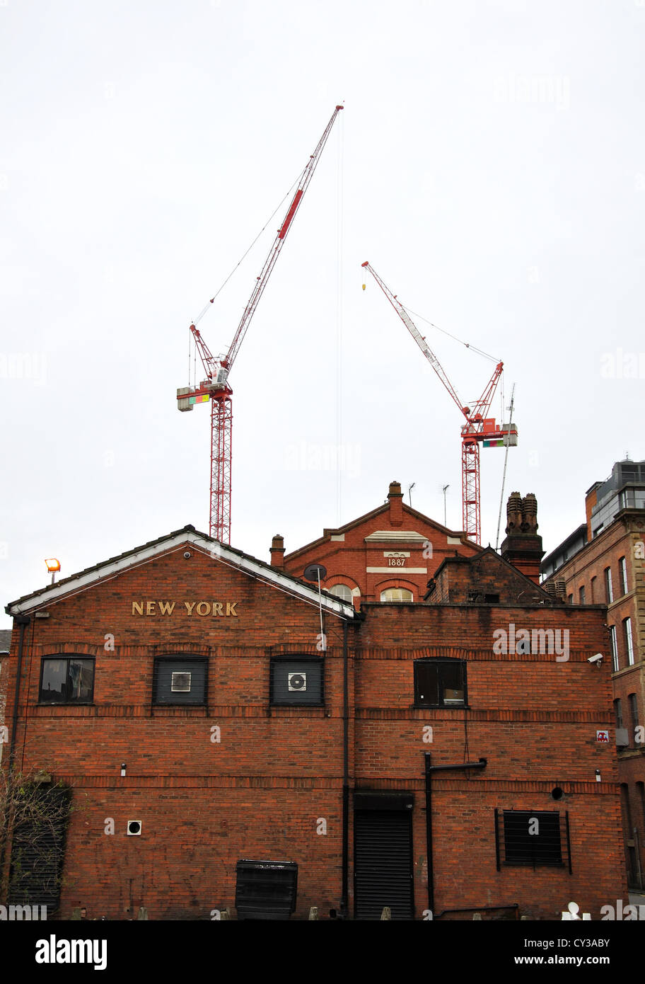 Fassade von einer kleinen alten Fabrik in Manchester mit Kränen hinter. UK, Großbritannien. Stockfoto