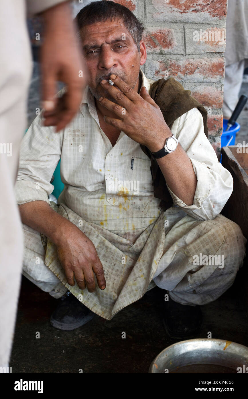 Eine Waza oder traditionellen Kashmiri Kochen raucht eine Zigarette während einer Pause in der Küche auf eine Wazwan fest. Srinagar, Kaschmir, Indien Stockfoto
