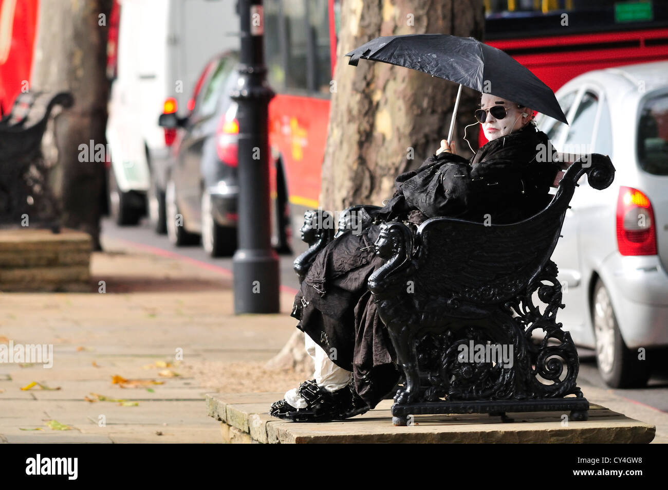 London, England, Vereinigtes Königreich. Mann in schwarz mit weißen Gesicht gekleidet und mit Sicherheitsnadeln, mit einem Regenschirm an einem sonnigen Tag Stockfoto