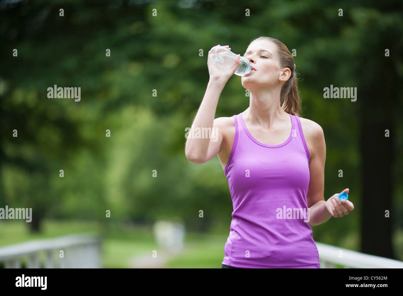 Junge Frau zu Fuß über die Brücke und Trinkflasche mit Wasser nach dem Joggen Stockfoto