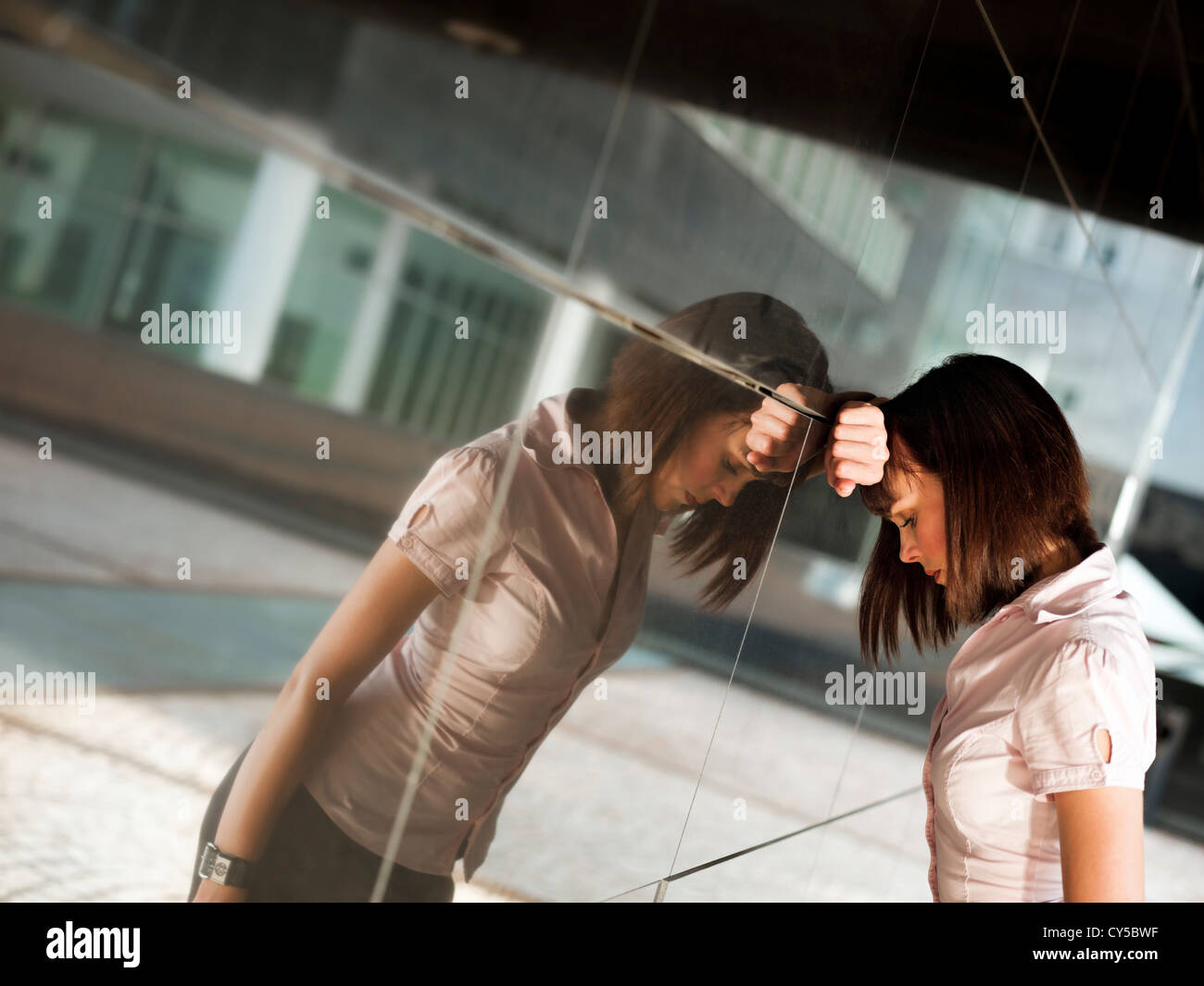 traurig kaukasischen Geschäftsfrau, schlug den Kopf gegen eine Wand aus Bürogebäude. Reflexion an Wand Stockfoto