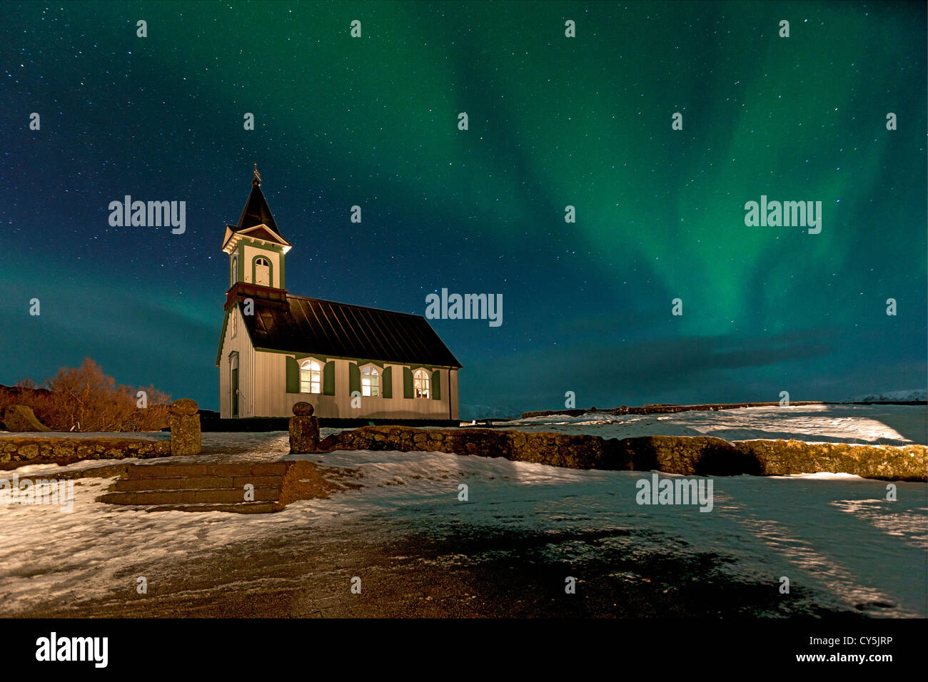 Beleuchtete isländischen Kirche nachts im Schnee mit hellen Aurora Borealis overhead Stockfoto