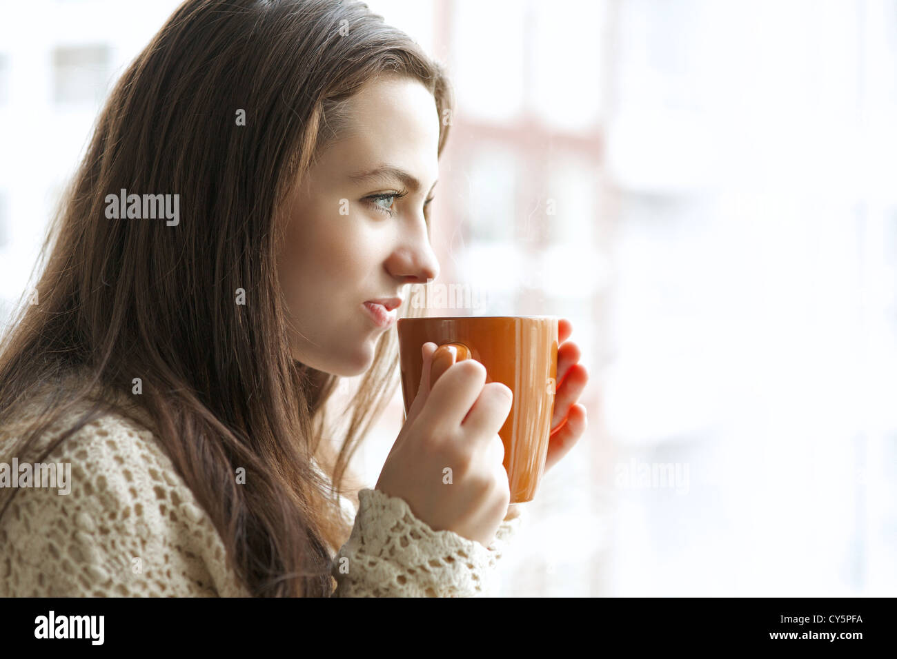 Schöne junge Mädchen trinken heißen Tee beim Blick auf das Fenster Stockfoto