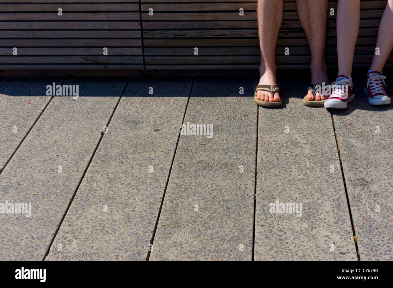 Die Füße eines jungen Paares tragen Sommerschuhe sitzend auf einem Bleicher im der High Line Park City, Manhattan, New York. Stockfoto