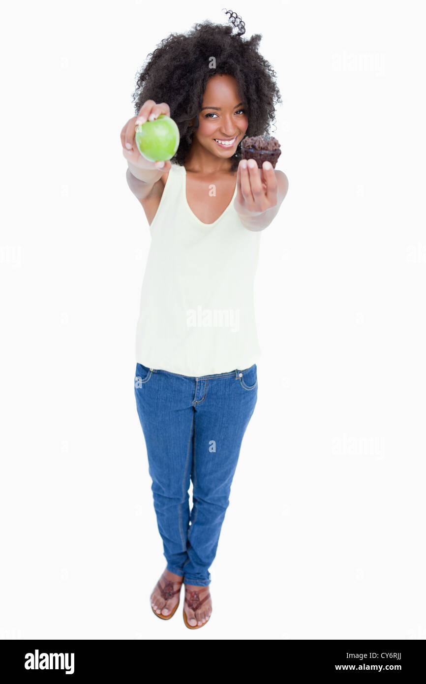 Lächelnde junge Frau hält einen Apfel in der einen Hand und einem Muffin in der anderen Stockfoto