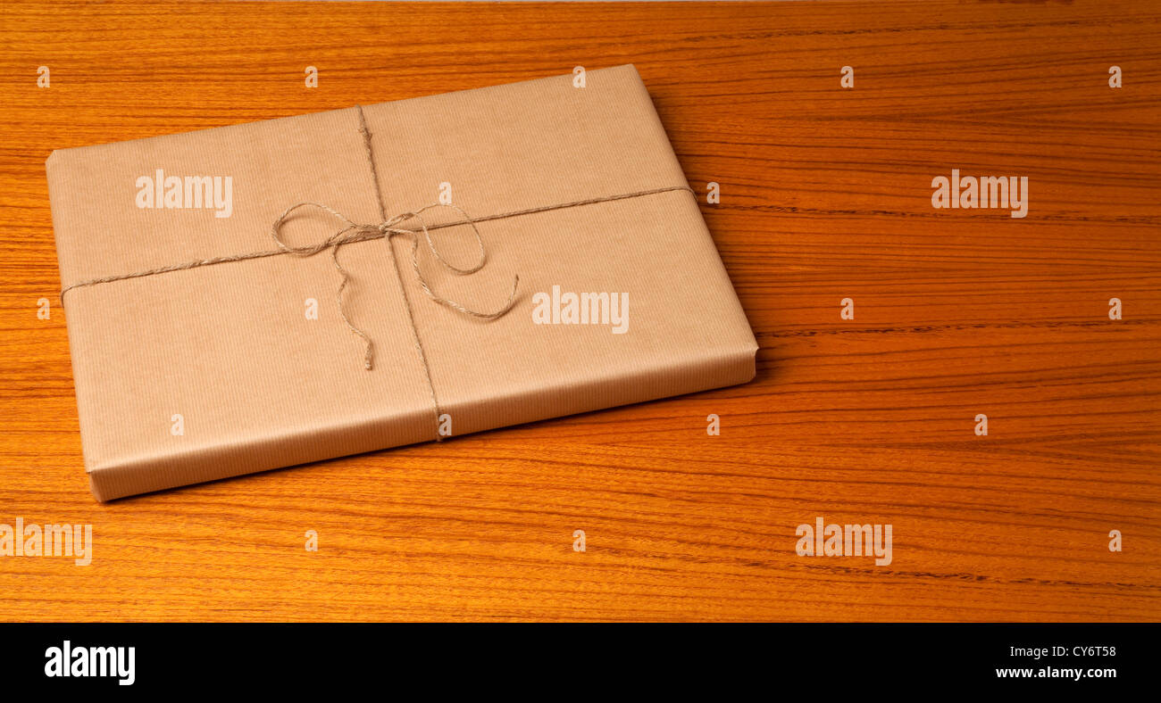 eine braune Geschenk-Paket mit einer Zeichenfolge und einem Bogen auf einem Holztisch mit Körnung Muster Studioaufnahme. Paket auf der linken Seite. Stockfoto