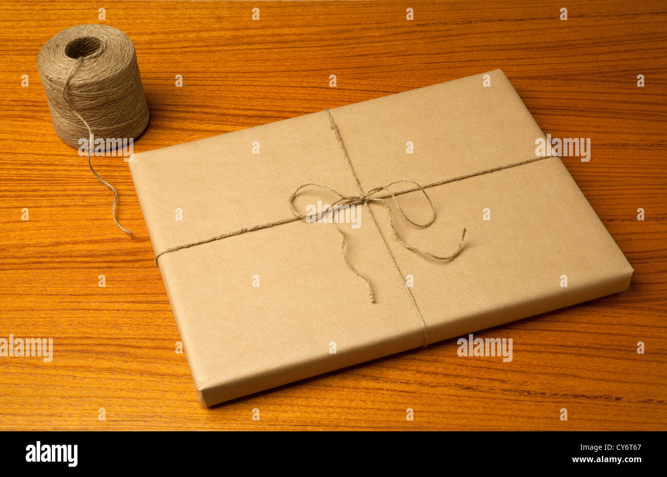 braune Geschenk-Paket mit einer Zeichenfolge und einem Bogen und einer Zeichenfolge Spule auf einem Holztisch mit Körnung Muster Stockfoto