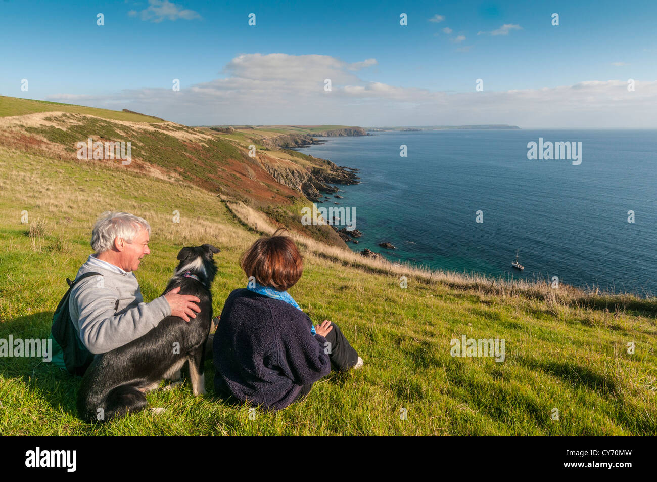 Ein Paar und ihr Hund genießen an einem späten sonnigen Sommerabend die Aussicht auf den Küstenweg South Devon östlich von Plymouth. GROSSBRITANNIEN Stockfoto